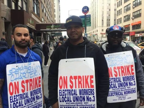 (From l.) IBEW Local 3 members Philip Sclafani, Jesus de la Cruz and Ayobami Ojedapo walk the picket line Friday outside Charter Communications' E. 23rd St. headquarters.